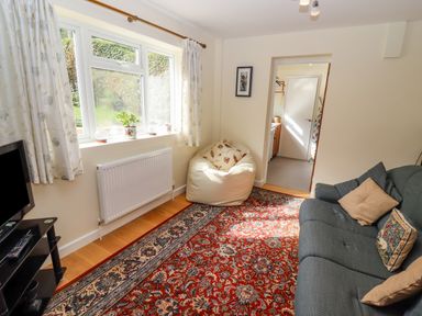 A living room with a blue sofa and a bean bag chair next to a window with curtains and a red patterned rug on wooden floor at The Gables in Sheepscombe