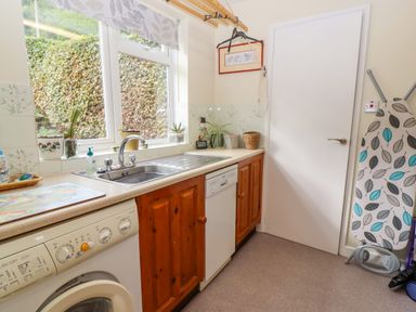 A laundry room with a washing machine and dishwasher under a counter next to a window an ironing board and a door at The Gables in Sheepscombe