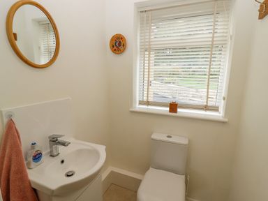 A small bathroom with a sink a mirror a toilet and a window with blinds at The Gables in Sheepscombe