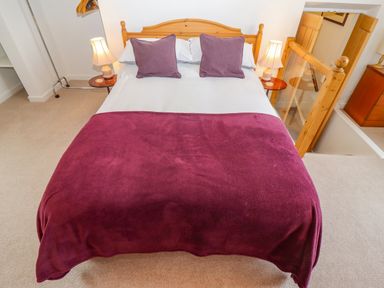 A bedroom with a double bed with purple pillows and blanket two bedside tables with lamps and a wooden staircase at The Gables in Sheepscombe