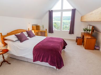 A bedroom with a double bed and purple bedding with a wooden dresser and large window at The Gables in Sheepscombe