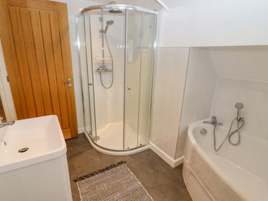 A bathroom with a shower enclosure, bathtub, sink, wooden door, and a rug on the floor at The Gables in Sheepscombe
