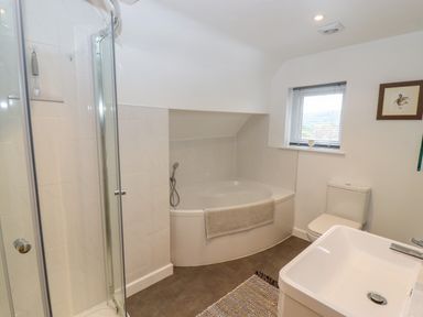 A bathroom with a corner bathtub a shower cubicle a toilet a sink and a small window at The Gables in Sheepscombe
