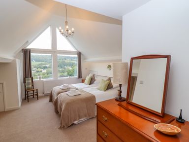 A bedroom with two single beds a wooden dresser with a mirror and a chair by a large window at The Gables in Sheepscombe