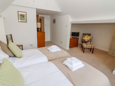 A bedroom with two beds with folded towels on them a chair with a pillow a small dresser with a TV and a lamp at The Gables in Sheepscombe