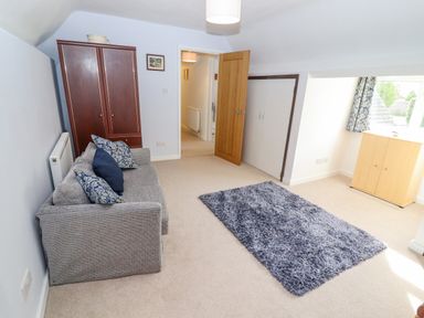 A room with a gray sofa with pillows a wooden wardrobe a wooden cabinet a blue rug and an open wooden door at The Gables in Sheepscombe