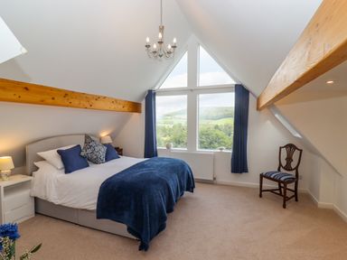 A bedroom with a bed a chair and large triangular window showing a view at The Gables in Sheepscombe