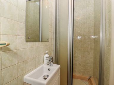 A small bathroom with beige tiled walls a white sink with hand soap a mirror above it and a shower with a sliding door