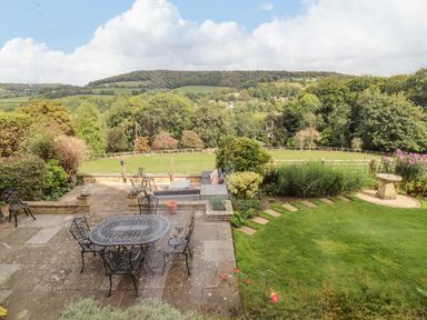A garden patio with a metal table and chairs and a seating area overlooking a lawn and countryside at The Gables in Sheepscombe