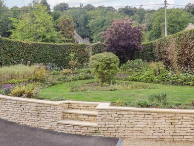 A garden with a stone retaining wall and steps surrounded by hedges and trees at The Gables in Sheepscombe