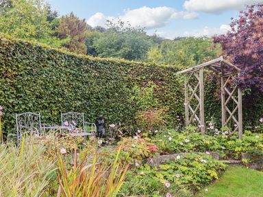 A garden with metal chairs a wooden arch and various plants in front of a hedge at The Gables in Sheepscombe