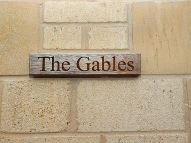 A wooden name plaque mounted on a stone wall with the words The Gables