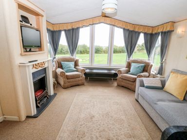 A living room with two armchairs and a sofa around a fireplace with a TV mounted above at Plas Tirion Caravan Llanfairynghornwy near Cemaes Bay