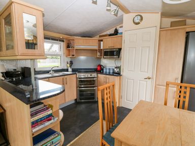 A kitchen with wooden cabinets a dining table with chairs and a window at Plas Tirion Caravan in Llanfairynghornwy near Cemaes Bay