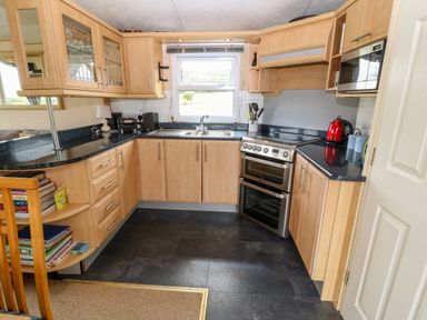 A kitchen with wooden cabinets black countertops a double oven a window and various appliances at Plas Tirion Caravan in Llanfairynghornwy near Cemaes Bay