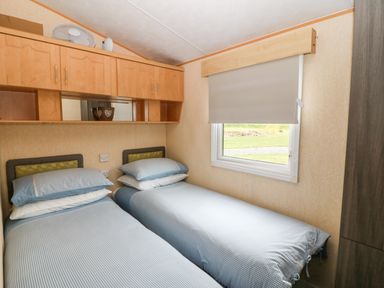 A bedroom with two single beds under a window with a blind and wooden cabinets above the beds at Plas Tirion Caravan Llanfairynghornwy near Cemaes Bay