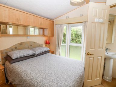A bedroom with a bed pillows curtains red lamp and a basin behind a door at Plas Tirion Caravan Llanfairynghornwy near Cemaes Bay