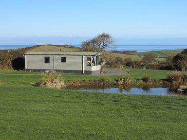 A mobile home near a small pond with green fields and trees in the background at Plas Tirion Caravan Llanfairynghornwy near Cemaes Bay