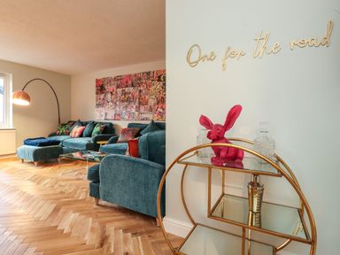 A living room with blue sofas a floor lamp and a wall art with a bar cart and pink rabbit figure at Tipsy Bee in Bowness-On-Windermere