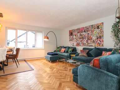 A living room with teal sofas colorful cushions glass coffee table and wall art at Tipsy Bee in Bowness-On-Windermere