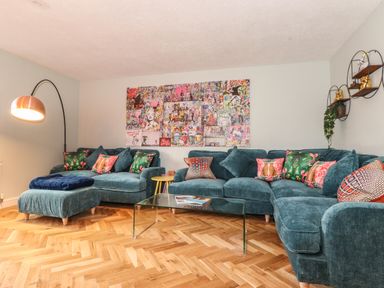 A living room with blue sofas colorful cushions glass coffee table and wall art at Tipsy Bee in Bowness-On-Windermere