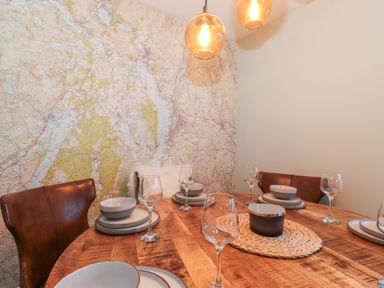 A dining area with a wooden table set with dishes and wine glasses brown leather chairs and a map wallpaper at Tipsy Bee in Bowness-On-Windermere