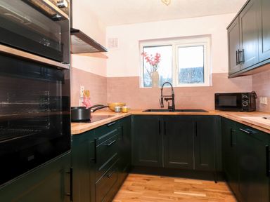 A kitchen with dark green cabinets wooden countertops a sink under a window and an oven at Tipsy Bee in Bowness-On-Windermere