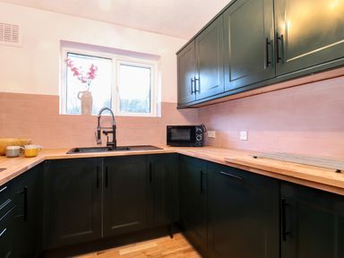 A kitchen with black cabinets wooden countertops a black sink a window with a vase of flowers and a microwave at Tipsy Bee in Bowness-On-Windermere