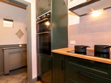 A kitchen with dark green cabinets two black pots on a stove and hanging mirrors in the adjoining room at Tipsy Bee in Bowness-On-Windermere