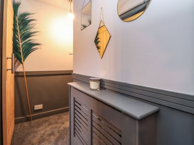 A hallway with a wooden door a tall green decorative feather a gray radiator cover with a candle on top and three mirrors on the wall at Tipsy Bee in Bowness-On-Windermere