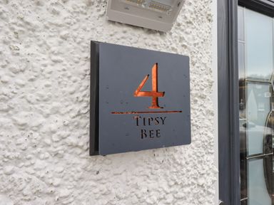 A metal house number sign with the number 4 and the words Tipsy Bee on a textured white wall at Tipsy Bee in Bowness-On-Windermere