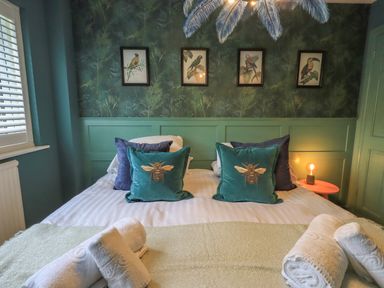 A bedroom with a double bed green bee cushions wall art of birds and rolled white towels on the bed at Tipsy Bee in Bowness-On-Windermere