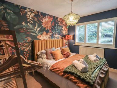 A bedroom with a bed with folded towels and pillows and a floral accent wall at Tipsy Bee in Bowness-On-Windermere