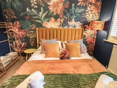 A bedroom with a double bed with patterned pillows and a floral wallpaper at Tipsy Bee in Bowness-On-Windermere