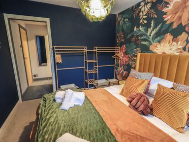A bedroom with a bed covered in pillows and blankets and a floral wallpaper at Tipsy Bee in Bowness-On-Windermere