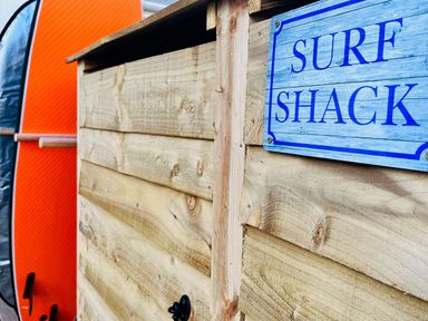 A surf shack with a wooden structure and a surfboard at Kippy Cottage Porthtowan