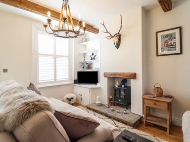 A living room with a sofa a wood stove a television and wooden beams at Glynside in Conwy