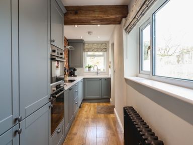 A kitchen with blue cabinets wooden floor a window and a black radiator at Glynside in Conwy