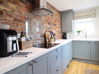 A kitchen with blue cabinets a brick wall a white countertop and appliances at Glynside in Conwy