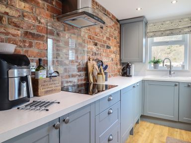 A kitchen with blue cabinets a black air fryer a wooden box with bottles cooking utensils a stove a window and a sink at Glynside in Conwy