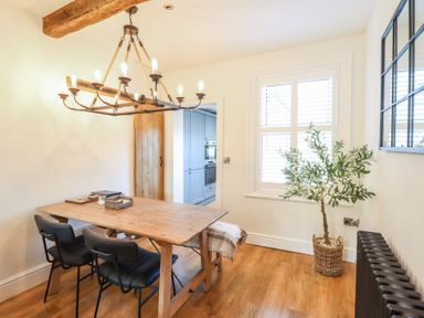 A dining area with a wooden table and black chairs under a chandelier near a window with shutters and a potted plant at Glynside Conwy