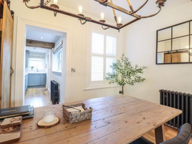 A dining room with a wooden table a plant in the corner and view into a kitchen at Glynside in Conwy