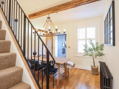 A dining area with a wooden table and black chairs next to carpeted stairs at Glynside in Conwy