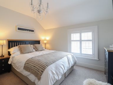 A bedroom with a bed with pillows and a striped throw blanket bedside tables with lamps a window with shutters and a chandelier at Glynside in Conwy