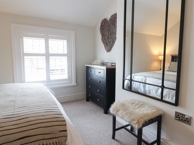 A bedroom with a bed with striped blanket a black dresser a wall mirror and a bench with fur cover at Glynside in Conwy