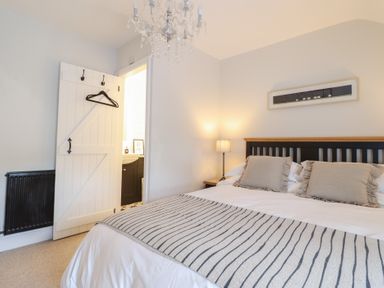 A bedroom with a bed a bedside table with a lamp a chandelier and a door leading to a bathroom at Glynside Conwy