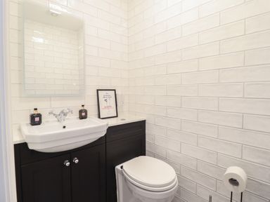 A small bathroom with a white sink and toilet a mirror above the sink and a framed sign on the counter at Glynside in Conwy