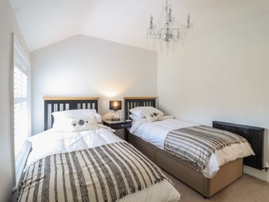 A bedroom with two single beds a nightstand with a lamp a window with shutters and a chandelier at Glynside in Conwy