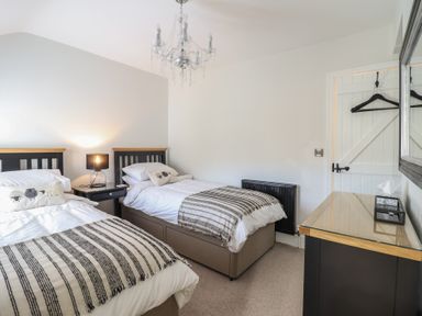 A bedroom with two single beds a bedside table with lamp and a dresser with a mirror at Glynside in Conwy