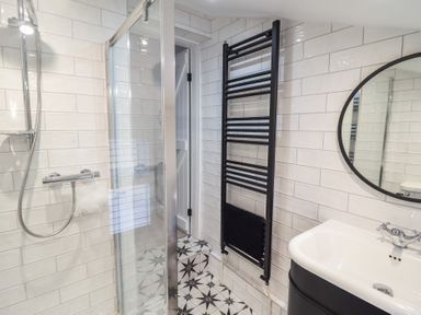 A bathroom with a shower area, black towel radiator, sink with a mirror above it, and patterned floor tiles at Glynside in Conwy